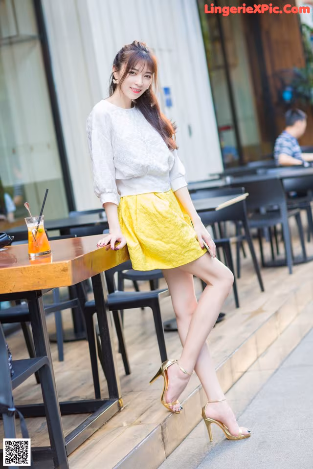 A woman in a white shirt and yellow skirt posing for a picture.