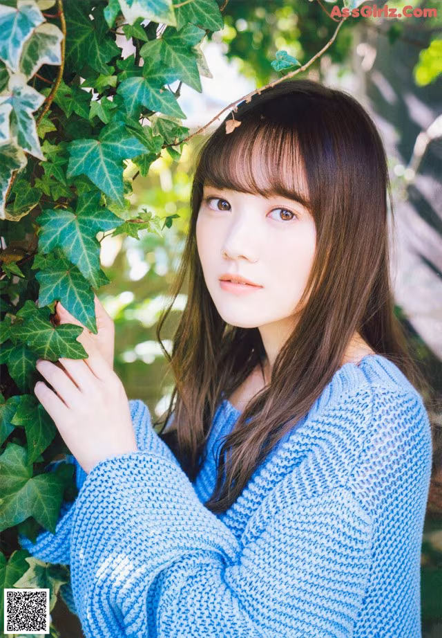 A woman in a blue sweater leaning against a tree.