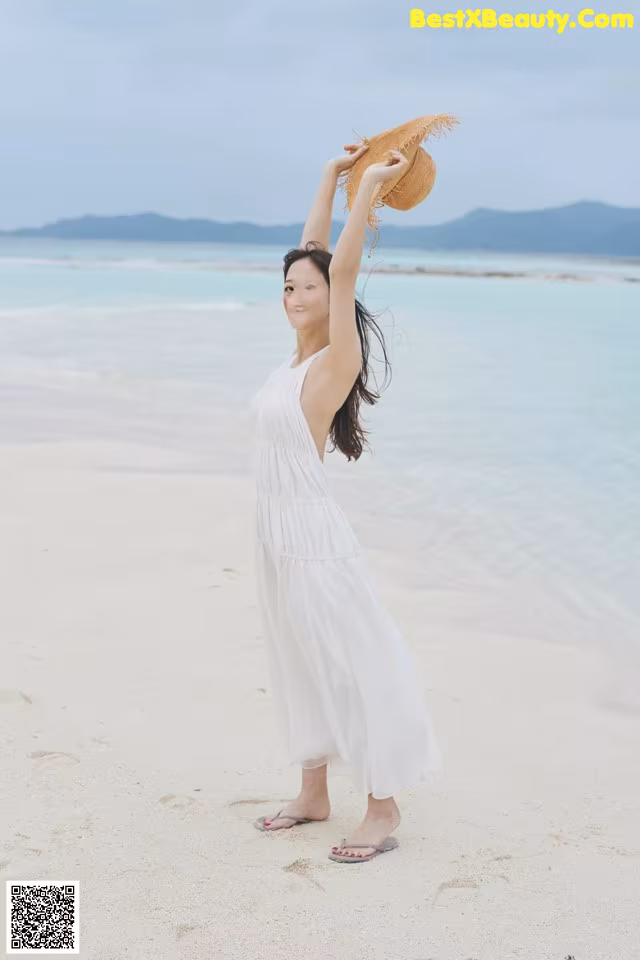 A woman in a white dress and straw hat on the beach.