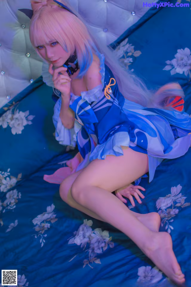 A woman in a blue and white dress sitting on a bed.