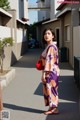 A woman in a purple and orange kimono standing on a sidewalk.