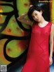 A woman in a red dress leaning against a graffiti wall.