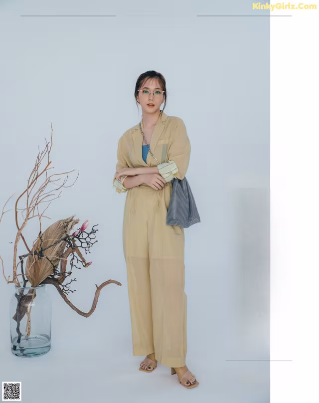 A woman standing in front of a vase with branches in it.