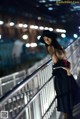 A woman in a black dress and hat standing on a bridge.