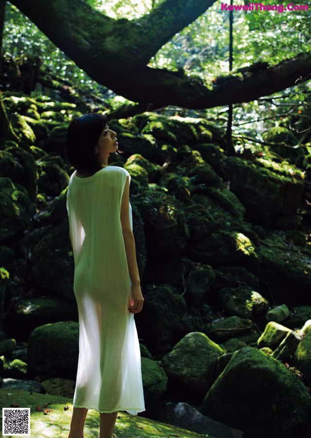 A woman in a white dress standing in the woods.