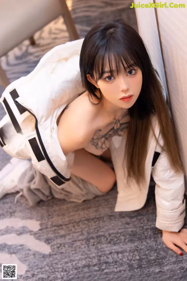 A woman in a white jacket leaning against a wall.