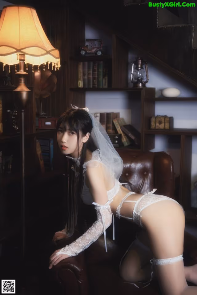 A woman in a white lingerie sitting on a brown chair.