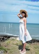 A woman in a white dress and straw hat standing on a beach.