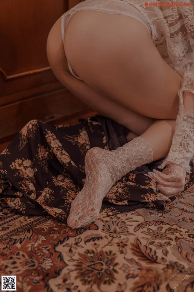 A woman in a white lingerie sitting on a rug.
