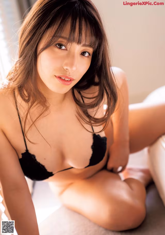 A woman in a black bra sitting on a white couch.