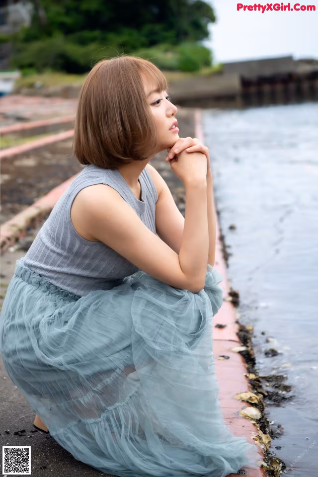 A woman sitting on the edge of a body of water.